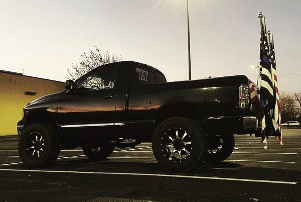 Black lifted pickup truck in a parking lot at dusk with two flags on a FanPole Double Barrel mount at the rear hitch