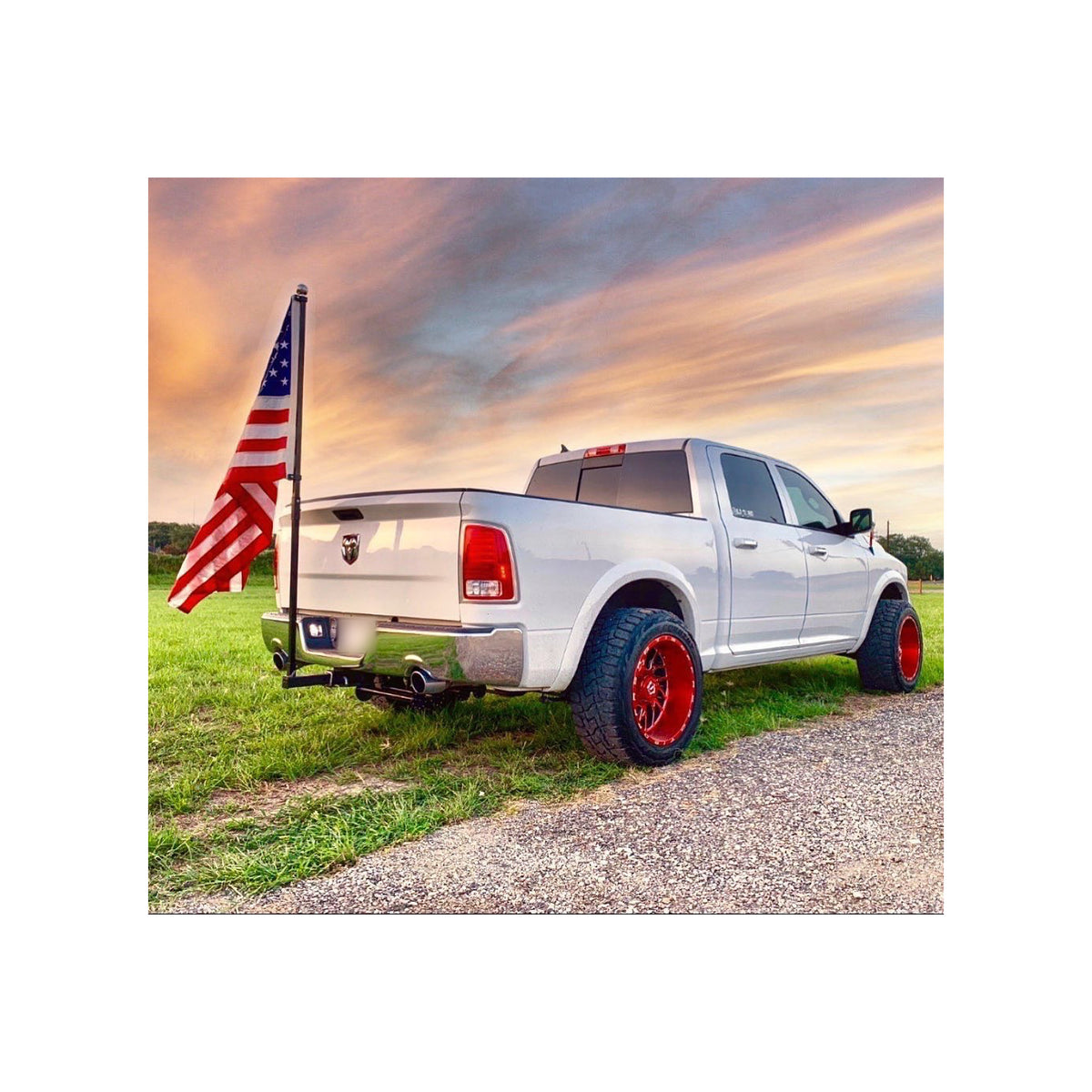 White pickup truck parked on grass at sunset with a FanPole flag pole mounted in its rear hitch receiver, flying a full-size American flag.