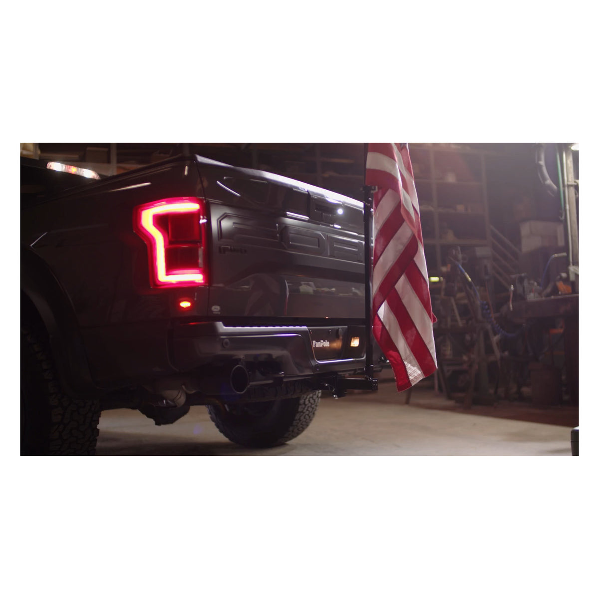 Close-up of a FanPole dummy hitch pinned into a truck's rear hitch receiver, with the steel pole holding a full-size American flag beside the tailgate.